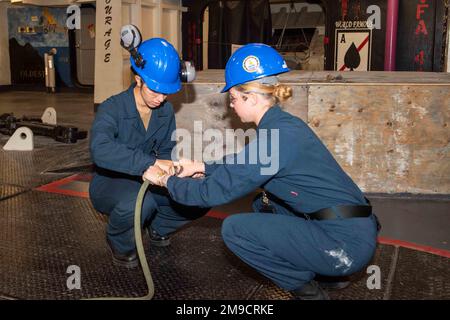 USA Navy Boatswain's Mate 3. Klasse Megan Sorg, rechts, aus Chicago und den USA Navy Seaman Katherine Nunez aus New York, beide dem Flugzeugträger USS John C. Stennis (CVN 74) zugewiesen, verbinden eine Schlauchleitung mit einem Schleifgerät an Bord des Schiffes, in Newport News, Virginia, 16. Mai 2022. John C. Stennis arbeitet in Newport News Shipyard zusammen mit NNS, NAVSEA und Auftragnehmern, die im Rahmen der Mission, das Kriegsschiff rechtzeitig und im Rahmen des Budgets wieder in den Kampf zurückzubringen, ihre Pflicht zur Verteidigung der Vereinigten Staaten wiederaufnehmen. Stockfoto