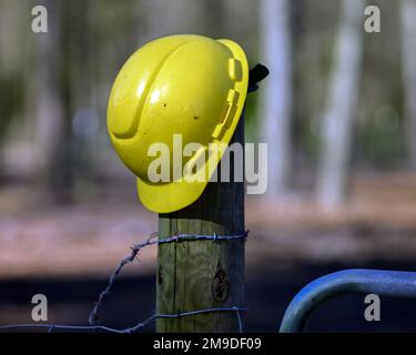 Ein gelber Bauarbeiter-Helm auf einem Zaunpfahl Stockfoto