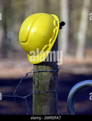 Ein gelber Bauarbeiter-Helm auf einem Zaunpfahl Stockfoto