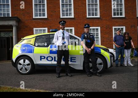 Zwei ehrenamtliche Polizeibeamte aus dem Vereinigten Königreich stehen an einem elektrisch angetriebenen Polizeifahrzeug der Royal Air Force während eines Autorentreffens in der Royal Air Force Mildenhall, England, am 17. Mai 2022. Mitglieder des Team Mildenhall begrüßten ehrenamtliche, pensionierte und aktive britische Polizei, um ihre Fahrzeuge zu Ehren der Polizeiwoche vorzuführen. Stockfoto