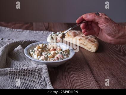 Weiblicher Handlöffel mit französischem Salat auf einem Holztisch Stockfoto