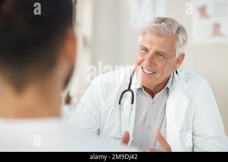 Ich habe gute Neuigkeiten für dich. Ein Oberarzt, der während einer Sprechstunde in seiner Klinik bei seinem Patienten sitzt. Stockfoto