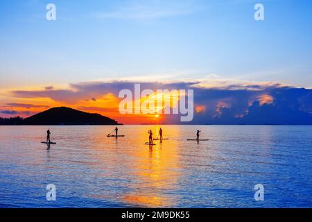 People Silhouettes Stand SUP Paddle Boarding, Sea Sunset Beach, aktiver junger Mann, Surfbrett, Ozean Sonnenaufgang, Surfbrett, Wassersport Stockfoto