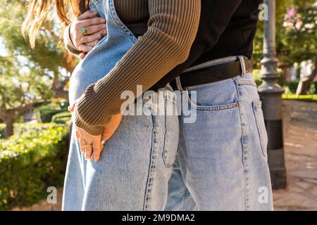 Geerntet, anonym, männlich in Jeans, berührt schwangeren Bauch von weiblich in Denim, steht auf der Straße an sonnigen Tagen Stockfoto