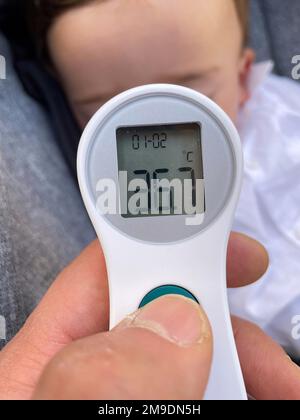 Eine vertikale Nahaufnahme der Hand eines Vaters, die die Temperatur eines Babys mit einem Thermometer misst Stockfoto