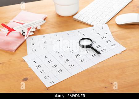 Kalender und Erinnerungen für Geschäftsreisen, Reisen und Urlaub. Gleiter auf dem Schreibtisch mit Flugzeug und Lupe, Stift und Tastatur. Markierung wichtig Stockfoto