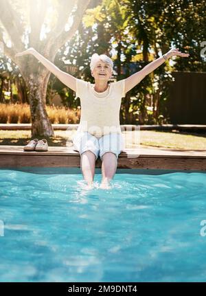 Seniorin, Lächeln und Füße im Swimmingpool, entspannen Sie sich für Sommerurlaub, Schwimmen oder Urlaubsfreuden in der Natur. Glückliche alte Frau mit Armen Stockfoto