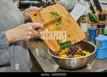 Der Küchenchef verwandelt das Gemüse in Salat mit Zucchini, Orangen und Salami. Französische Gourmetküche, Holzhintergrund. Stockfoto