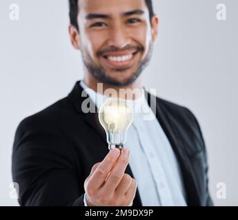 Ein junger Mann, der eine Glühbirne vor grauem Hintergrund hält. Stockfoto