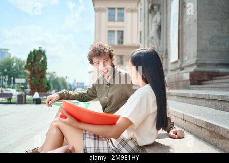 Ein paar Schüler mit Lehrbüchern, die auf der Treppe sitzen. Seitenansicht. Stockfoto