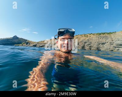 Männlicher Taucher schwimmt mit einer Maske und macht ein Selfie auf der Wasseroberfläche in der Natur Stockfoto