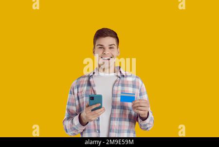 Glücklicher junger Mann mit Bankkarte und Handy, der online einkauft oder bezahlt Stockfoto