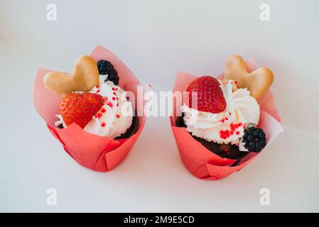 Cupcakes mit Sahne und frischen Erdbeeren und Brombeeren und herzförmigen Keksen auf weißem Hintergrund Stockfoto