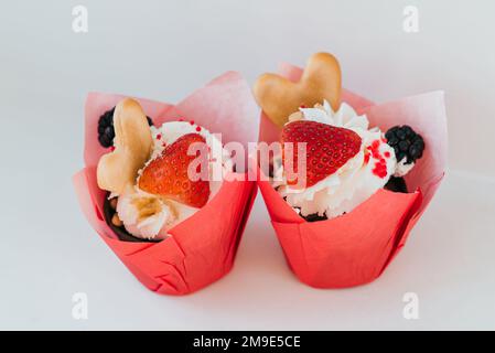 Cupcakes mit Sahne und frischen Erdbeeren und BlackBerry-Beeren und herzförmigen Plätzchen zum Valentinstag Stockfoto