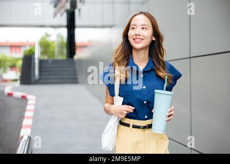 Geschäftsfrau, die selbstbewusst lächelt, mit einer Stofftasche, die eine Thermosflasche aus Stahl hält Becher Wasserglas Stockfoto