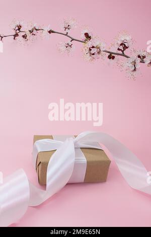 Zweig aus Kirsche, Aprikose, Sakura mit Geschenkbox mit Band auf pinkfarbenem Hintergrund. Feiertage, Internationaler Frauentag, Muttertag, Geburtstag, 8. März. Stockfoto