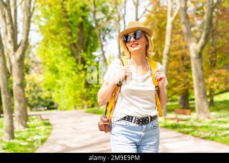 Eine touristische blonde Frau mit Hut und Sonnenbrille, die im Frühling einen Park in der Stadt besucht, Ecken des Parks kennenlernt und Fotos macht Stockfoto