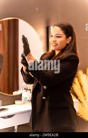 Frau lateinamerikanischer Abstammung in einem ästhetischen Augenbrauen- und Nagelladen. Porträt einer Chefin, die Handschuhe anzieht Stockfoto