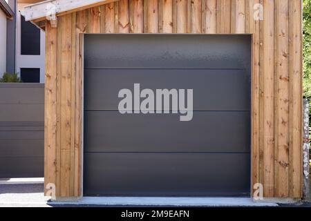 Moderne Garagentür in dunkelgrauem Holzgebäude Stockfoto