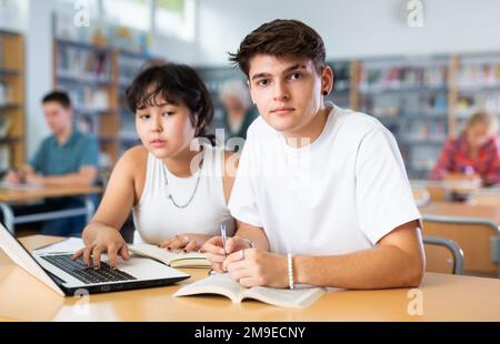 Asiatische Schülerin mit Klassenkamerad Kerl, studieren auf einem Laptop und Notizen in einem Copybook Stockfoto