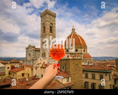 Eine Frau hält einen Aperol Spritz Cocktail mit Blick auf den Dom oder die Cattedrale di Santa Maria del Fiore in Florenz, Italien Stockfoto