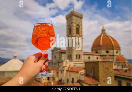 Eine Frau hält einen Aperol Spritz Cocktail mit Blick auf den Dom oder die Cattedrale di Santa Maria del Fiore in Florenz, Italien Stockfoto