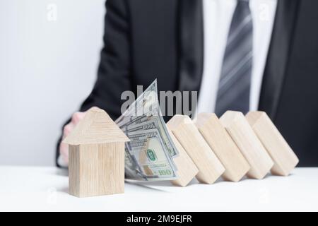 Holzhaus unter Geldschutz, Domino, Versicherungssicherheit Eigentumskonzept Stockfoto