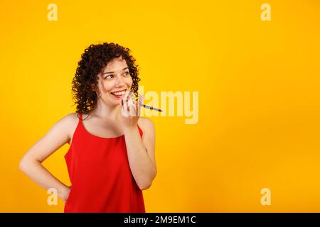Das süße, lockige Mädchen telefoniert. Eine junge Frau nimmt eine Sprachnachricht auf. Studio-weibliches Porträt auf hellgelbem Hintergrund