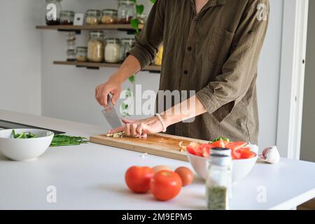 Nicht wiedererkennbarer junger asiatischer Mann, der Knoblauch schneidet. Stockfoto