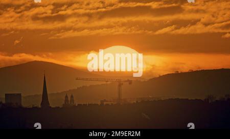 Glasgow, Schottland, Vereinigtes Königreich 18. Januar 2023. UK Weather: Kalter, klarer Himmel sah einen sehr kalten Start Red Dawn über dem Tinto Hill, dem höchsten Punkt im Zentrum Schottlands und mit Blick auf die Stadt. Einst der Spielplatz der Druiden, bekannt für seine Lagerfeuer und Menschenopfer, die vor Ort oft als Mount Doom bezeichnet werden und über den Bauflächen des neuen Glasgow-Universitätsgebäudes und dem Turm des Cottiers-Theaters in partick blickten. Credit Gerard Ferry/Alamy Live News Stockfoto