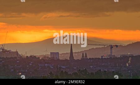 Glasgow, Schottland, Vereinigtes Königreich 18. Januar 2023. UK Weather: Kalter, klarer Himmel sah einen sehr kalten Start Red Dawn über dem Tinto Hill, dem höchsten Punkt im Zentrum Schottlands und mit Blick auf die Stadt. Einst der Spielplatz der Druiden, bekannt für seine Lagerfeuer und Menschenopfer, die vor Ort oft als Mount Doom bezeichnet werden und über den Bauflächen des neuen Glasgow-Universitätsgebäudes und dem Turm des Cottiers-Theaters in partick blickten. Credit Gerard Ferry/Alamy Live News Stockfoto