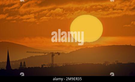 Glasgow, Schottland, Vereinigtes Königreich 18. Januar 2023. UK Weather: Kalter, klarer Himmel sah einen sehr kalten Start Red Dawn über dem Tinto Hill, dem höchsten Punkt im Zentrum Schottlands und mit Blick auf die Stadt. Einst der Spielplatz der Druiden, bekannt für seine Lagerfeuer und Menschenopfer, die vor Ort oft als Mount Doom bezeichnet werden und über den Bauflächen des neuen Glasgow-Universitätsgebäudes und dem Turm des Cottiers-Theaters in partick blickten. Credit Gerard Ferry/Alamy Live News Stockfoto