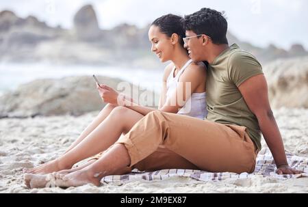 Sieh dir all die guten Bilder an, die wir haben. Ein junges Paar, das am Strand telefoniert. Stockfoto