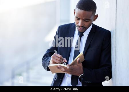 Meinen Geist mit meinem Tagebuch organisiert zu halten. Ein junger Geschäftsmann, der in der Stadt ein Tagebuch schreibt. Stockfoto