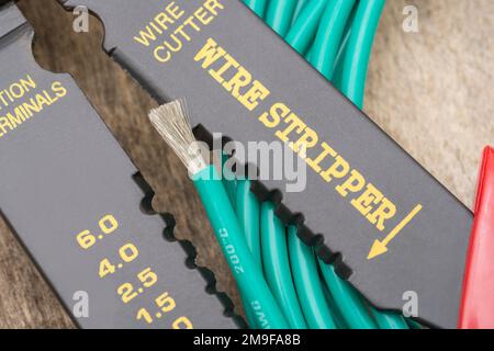 Nahaufnahme des in China hergestellten Abisolierers und Drahtschneiders ohne Markenkennzeichnung für 26-10AWG-Draht (siehe Hinweise) mit der Rolle eines grünen, silikonummantelten Drahts. Stockfoto