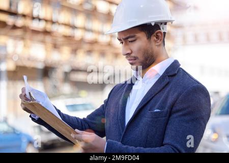 Arbeiten Sie sich von Grund auf durch. Ein Geschäftsmann, der auf einer Baustelle sein Klemmbrett überprüft. Stockfoto
