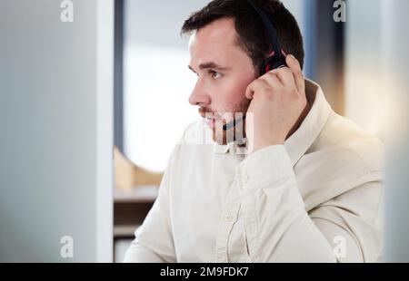 Könnten Sie das wiederholen? Ein attraktiver junger Callcenter-Agent, der allein in seinem Büro sitzt und bei der Verwendung seines Computers nachdenklich aussieht. Stockfoto