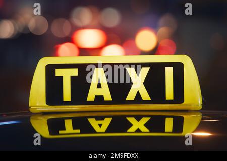 Gezielter Fokus auf Taxi-Schild auf dem Dach des Autos vor der geschäftigen Straße in der Stadt bei Nacht. Stockfoto