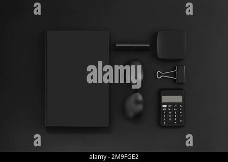 Kollektion von Bürozubehör in Schwarz auf Schwarz. Kreative monochrome Geschäftskomposition aus Notizblock, Brille, Taschenrechner, Puder, Lippenstift und Klo Stockfoto