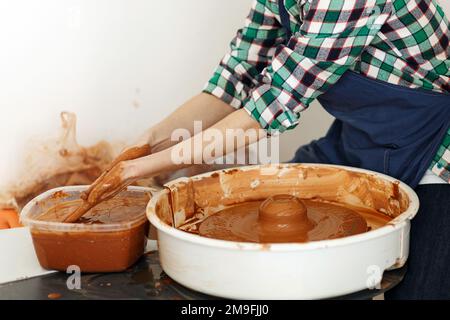 Zugeschnittenes Bild eines nicht wiedererkennbaren weiblichen Keramikmachers, das mit dem Keramikrad in Cozy Workshop arbeitet, macht eine Vase oder Tasse der Zukunft, kreatives Handwerk für Menschen Stockfoto