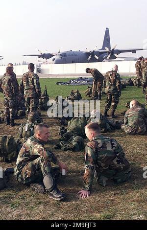 US-Armee-Soldaten der Delta Battery 319TH Airborne Unit, Vicenza, Italien, ruhen sich aus, reden und überprüfen ihre Ausrüstung, während sie auf ihren Trainingssprung warten, in der Maniago Air Drop Zone, nahe Aviano Air Base, Italien. Im Hintergrund steht ein Flugzeug der US Air Force C-130 Hercules aus dem 86. Wing Ramstein, Luftwaffenstützpunkt Deutschland. Stützpunkt: Luftwaffenstützpunkt Aviano Staat: Pordenone Land: Italien (ITA) Stockfoto