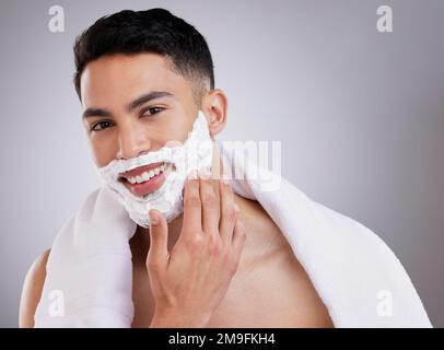 Stellen Sie sicher, dass die Zutaten hautsicher sind. Ein junger Mann, der Rasiercreme auf sein Gesicht aufträgt, vor einem Studiohintergrund. Stockfoto