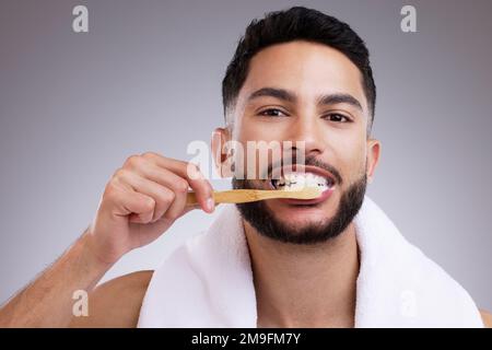 Blendet das Perlweiß selbstbewusst. Ein gutaussehender junger Mann putzt sich die Zähne vor einem Studiohintergrund. Stockfoto