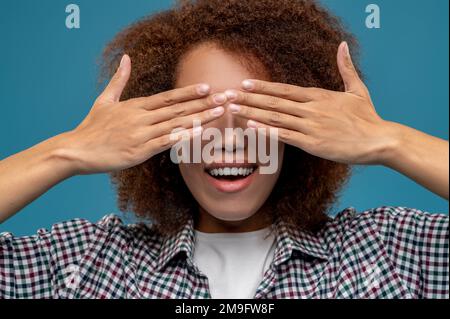 Eine junge Frau in einem karierten Hemd, die ihre Augen mit den Händen schließt Stockfoto