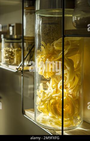 Regal mit Gewürzen und Pasten in großen Gläsern in Glasnähe an einer Küchenwand Stockfoto