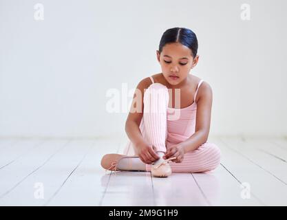 Meine Ballettschuhe geben mir magische Kräfte. Ein kleines Mädchen, das in einem Ballettstudio Schuhe anzieht. Stockfoto