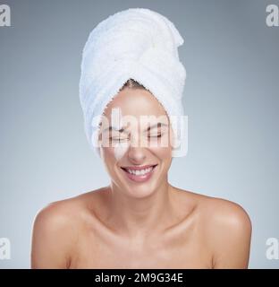 Sie liebt ihre neue Hautpflege. Studioaufnahme einer attraktiven jungen Frau mit einem Handtuch auf dem Kopf vor grauem Hintergrund. Stockfoto
