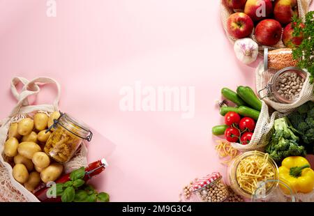 Blick von oben auf Glasgefäße mit Lebensmitteln und gemischten bunten frischen Rip gesundes Gemüse und Obst in umweltfreundlichen Baumwollsäcken auf rosa Rückseite Stockfoto
