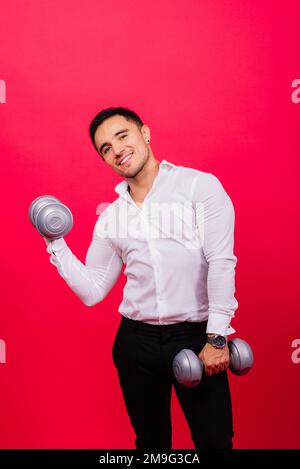 Geschäftsmann mit Fitness-Kurzhanteln trägt Hemd. Studioaufnahmen auf rotem Hintergrund Stockfoto