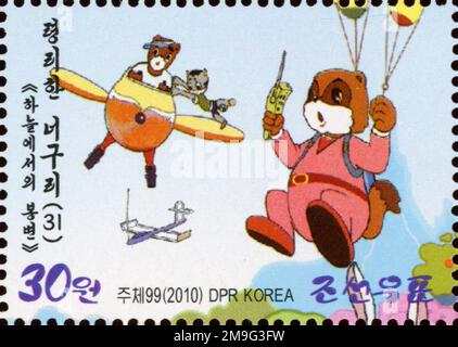 2010 Nordkorea Briefmarke mit Charakteren aus dem beliebten Zeichentrickfilm clever Raccoon Dog, der ein Flugzeug fliegt und Fallschirmspringen zeigt. Stockfoto